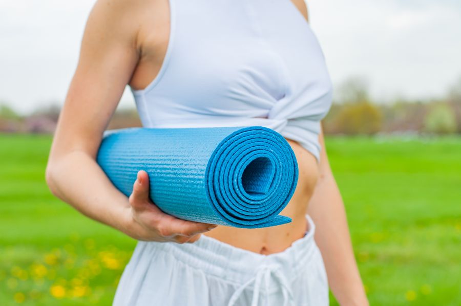 Woman holding a rolled yoga mat, ready to carry it to a session